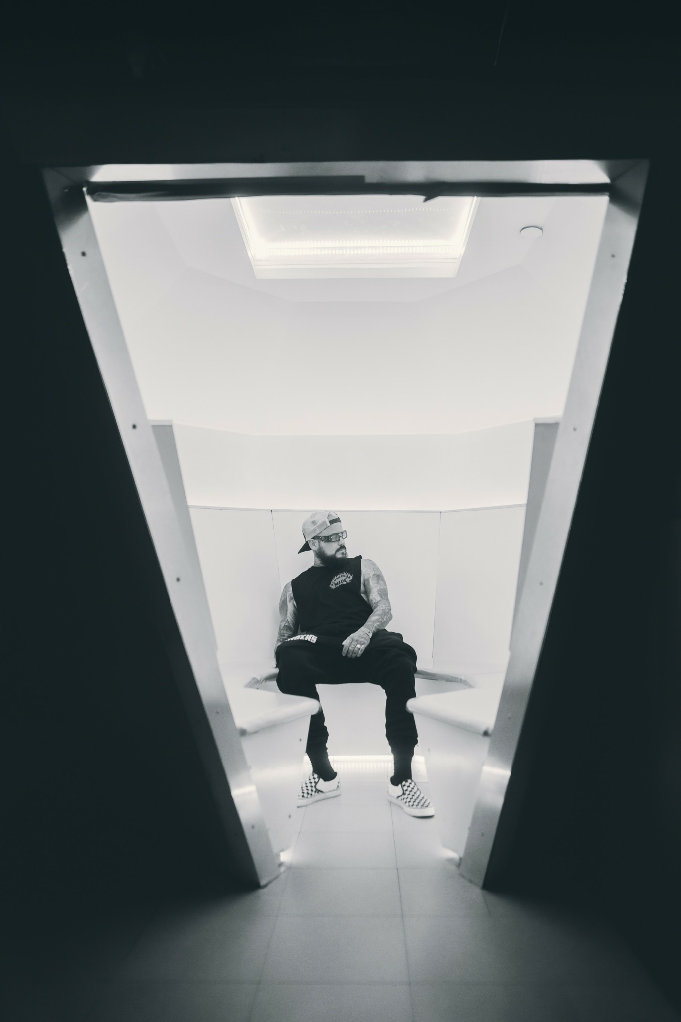 Person sitting on a chair in a small, illuminated room with a high ceiling, viewed through a doorway.
