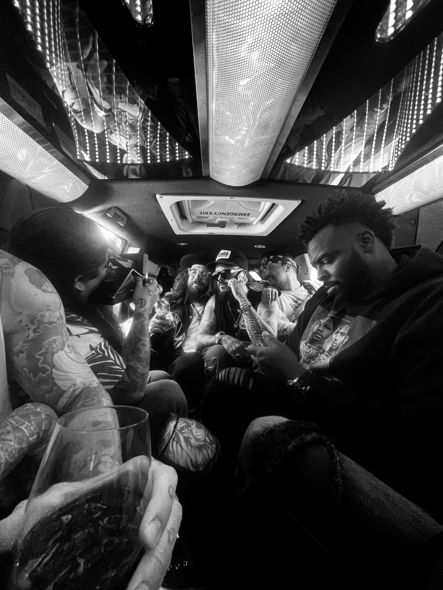People sitting inside a vehicle, some using phones, with reflective ceiling panels and a central light fixture.