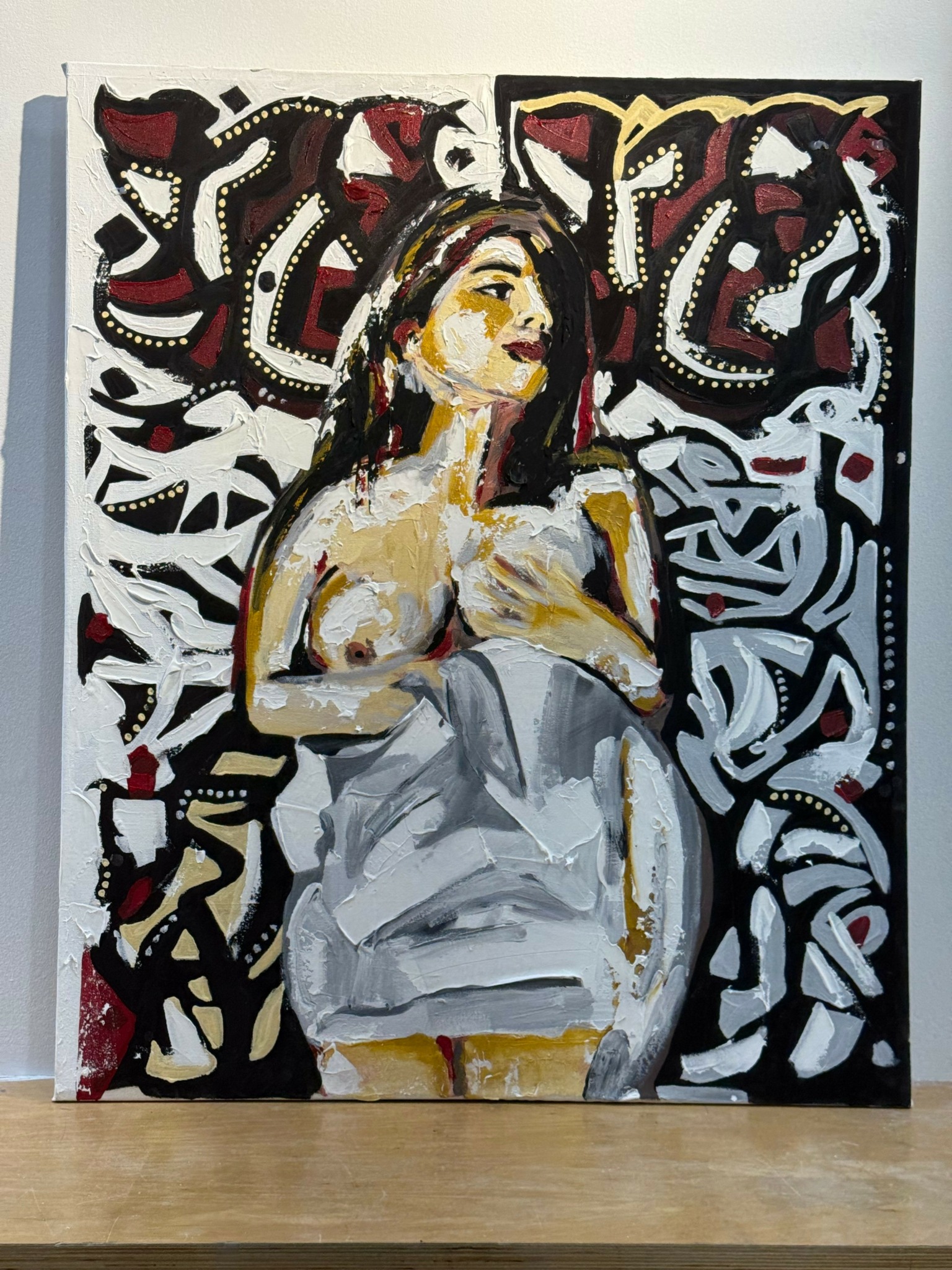 Painting of a woman with long hair, sitting with her arms crossed, surrounded by abstract black, white, red, and yellow patterns.