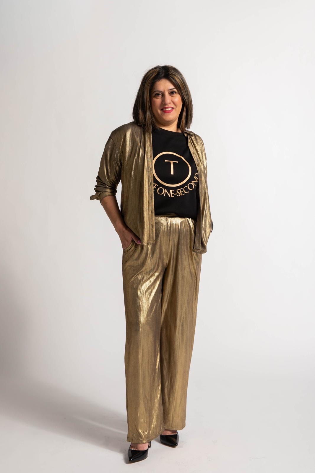 Woman with shoulder-length hair wearing a gold suit and black T-shirt, smiling, standing against a plain white background.