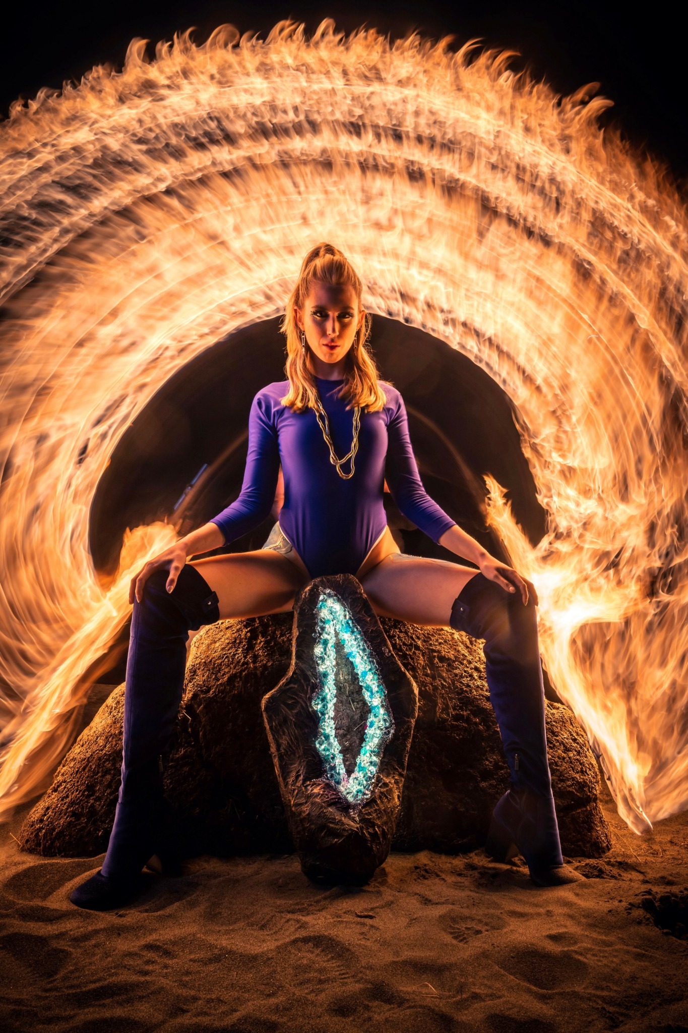 Woman in blue outfit sitting on a rock with fire spinning behind her, creating a circular flame pattern.