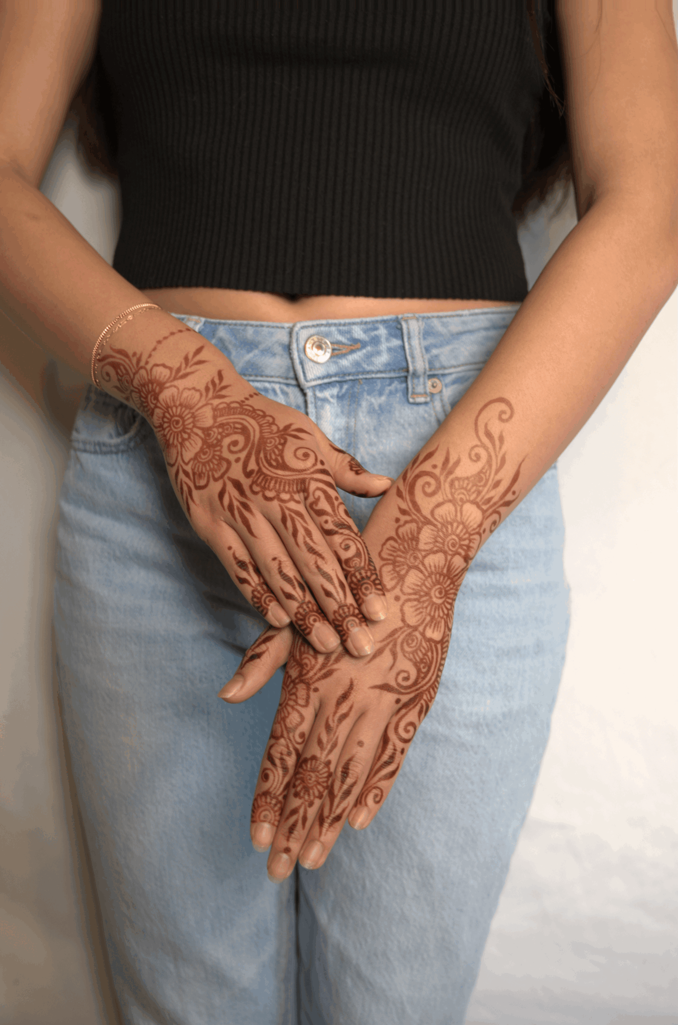 Person with intricate henna designs on hands and forearms, wearing a black top and light blue jeans.
