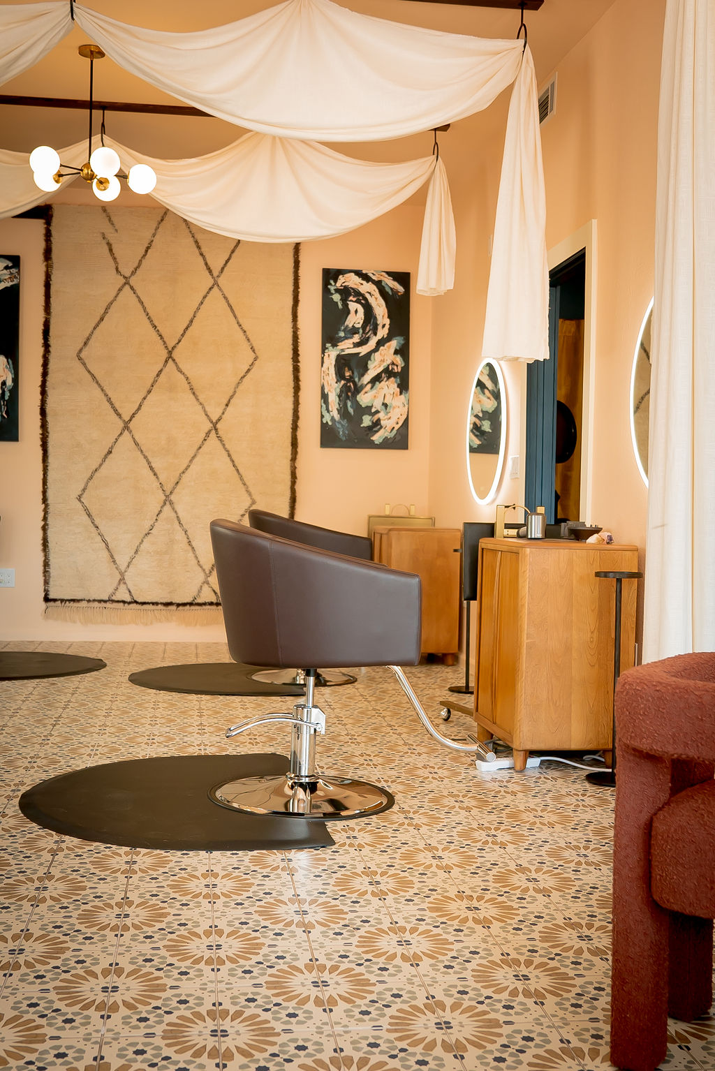 Interior room with vintage furniture, patterned carpet, and decorative wall art, featuring a salon chair and mirror.