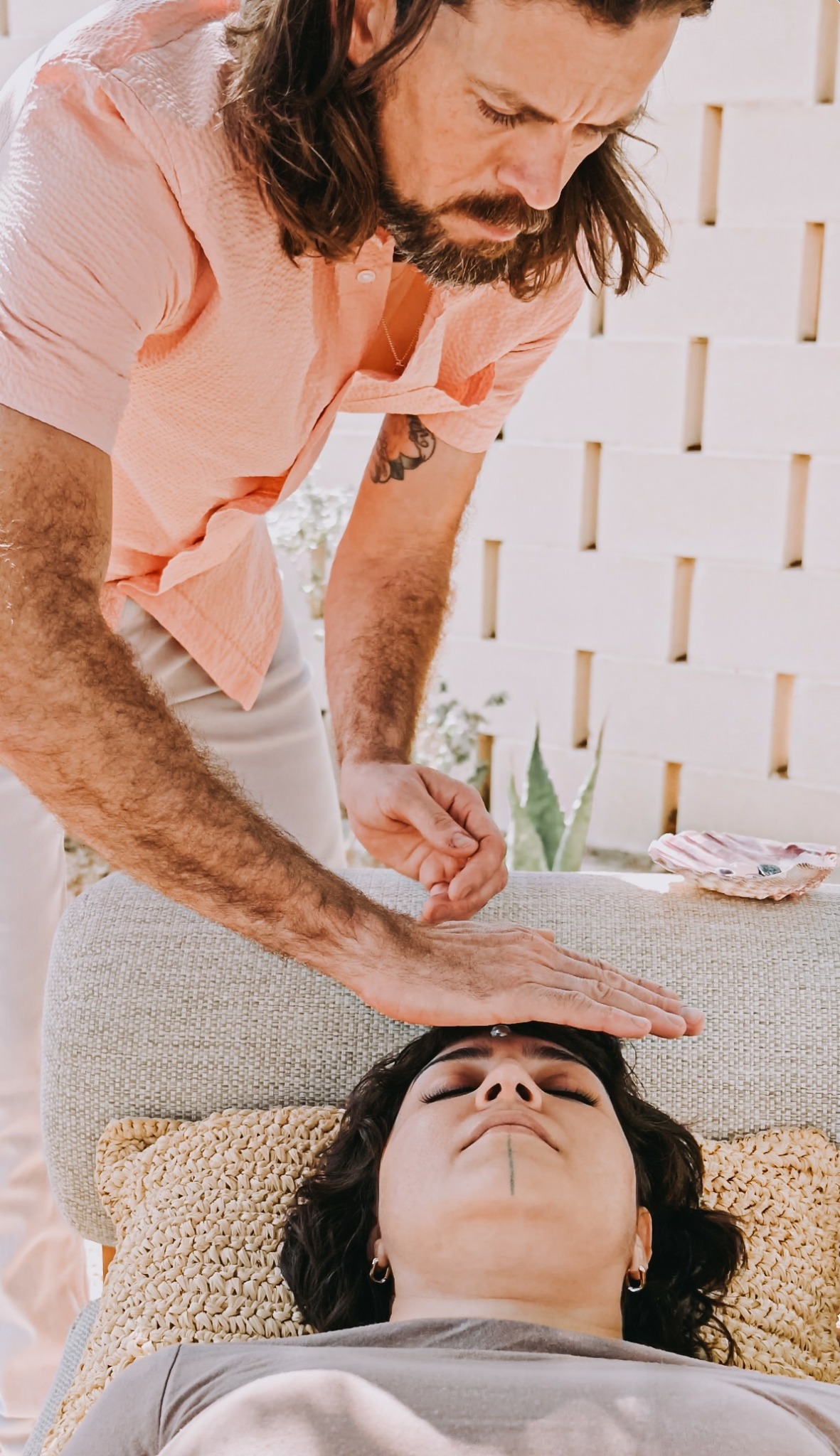 Man leaning over woman lying on a bed, with a white lattice wall in the background.