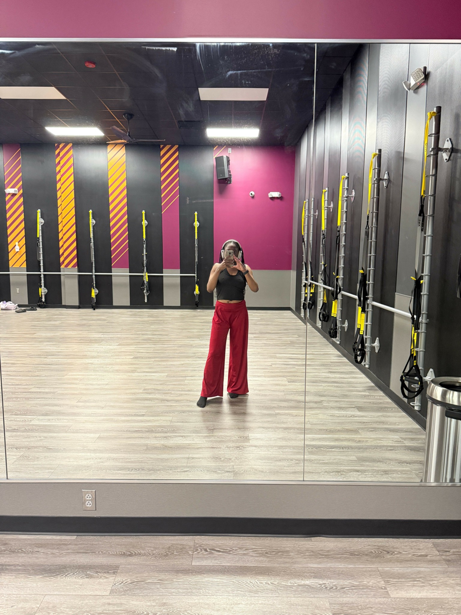 Person standing in a gym with black and pink walls, fitness equipment on the wall, and a light-colored floor.