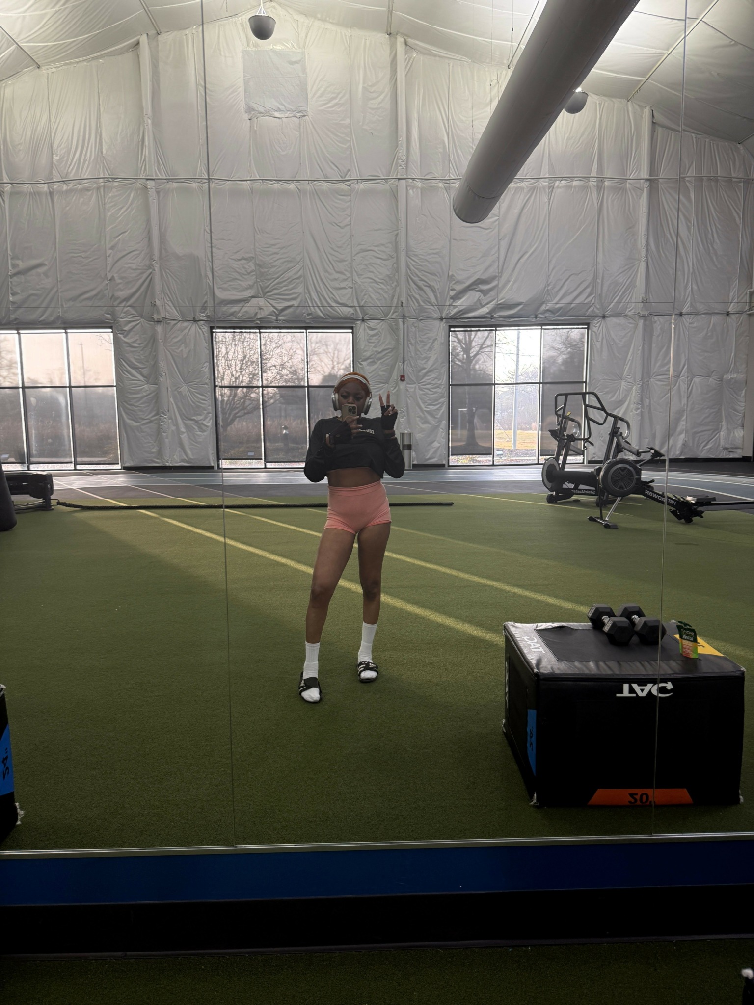 Person standing on tennis court with tennis racket, indoor sports facility, equipment, and net visible.