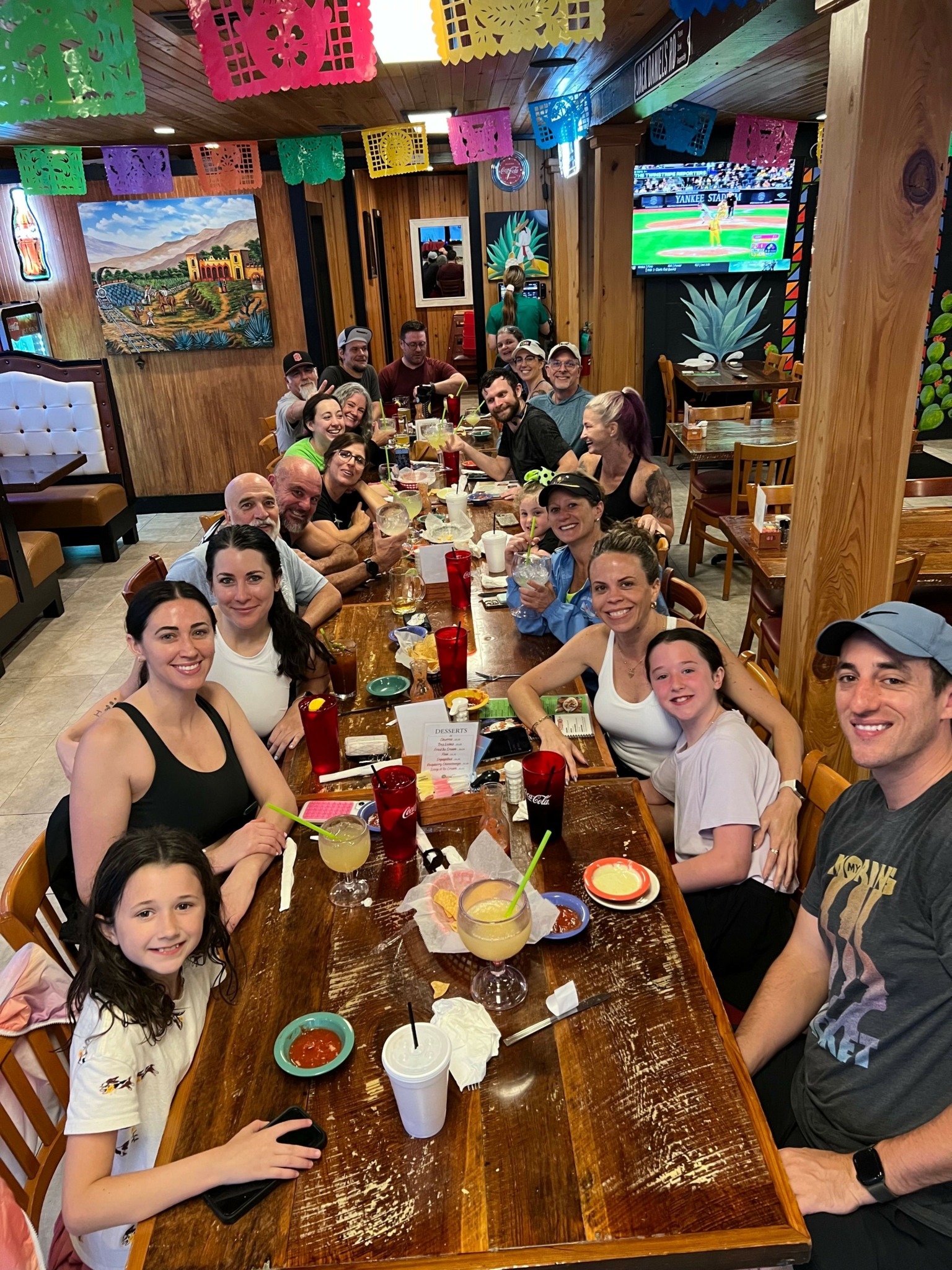 Group of people gathered around a long wooden table with food and drinks in a cozy, decorated room.