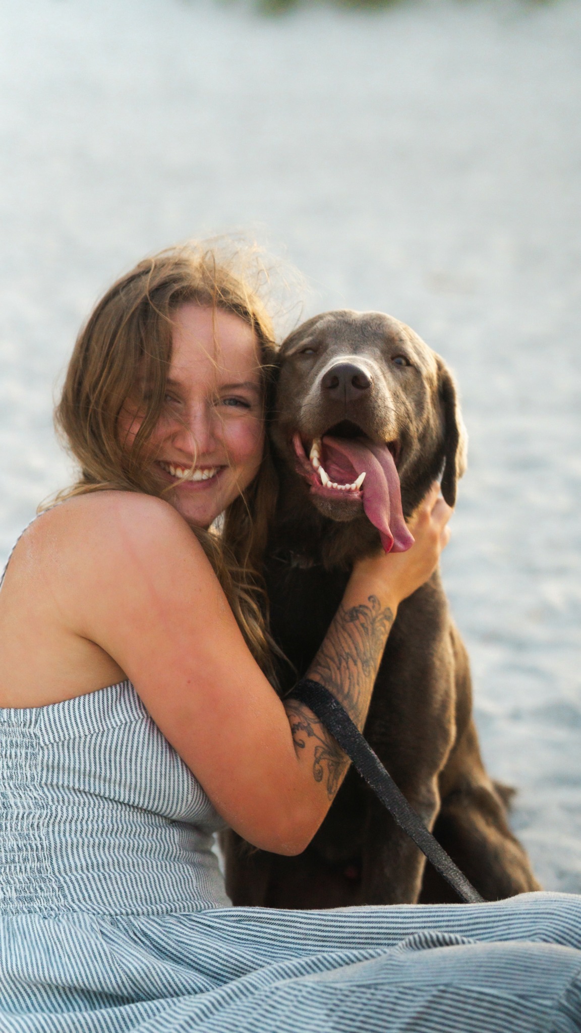 Woman smiling with a large dog outdoors near water, both looking happy and relaxed.