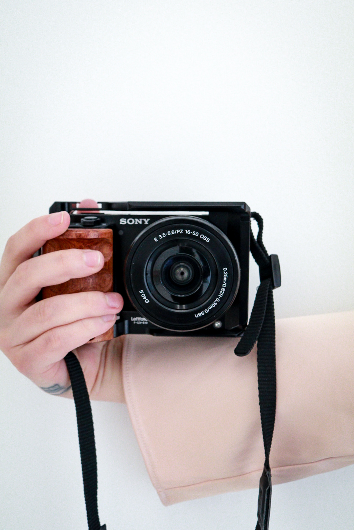 Person holding a black Sony camera with a strap, standing against a plain white background.