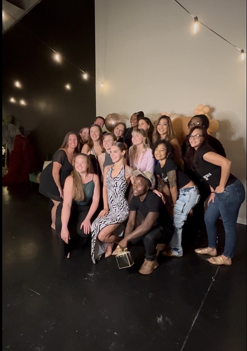 Group of women posing together in a dimly lit space with string lights overhead.