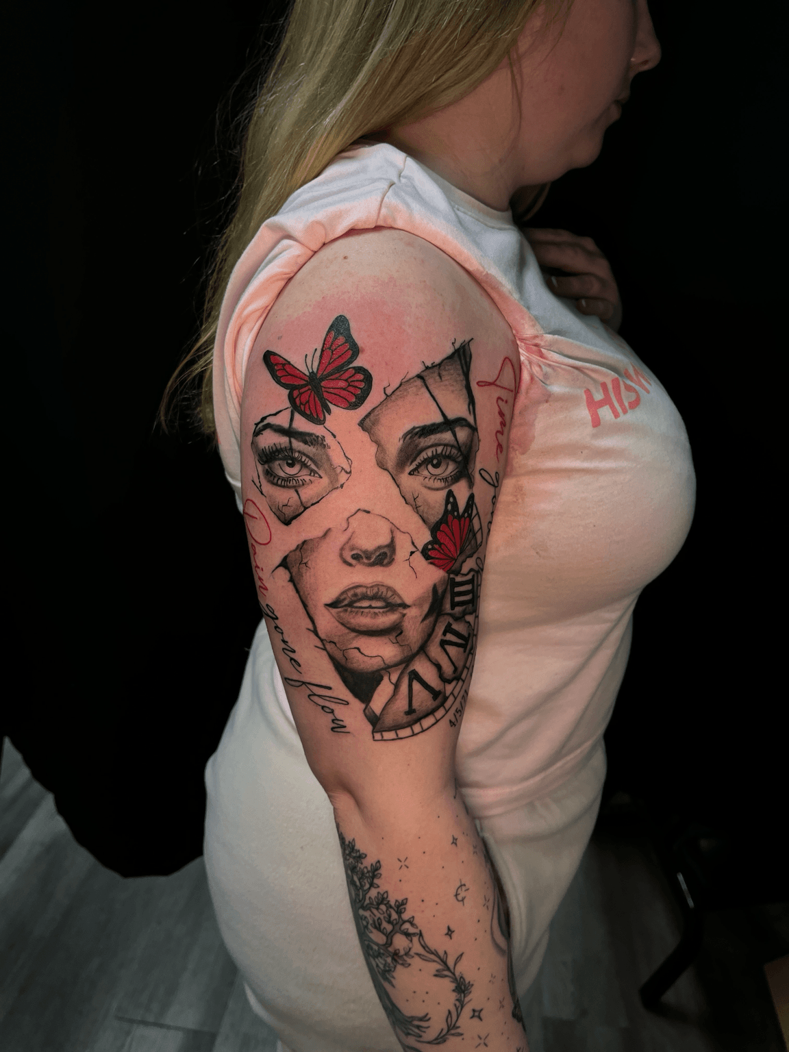 Side view of a woman with a colorful tattoo of a woman's face, butterflies, and text on her upper arm.