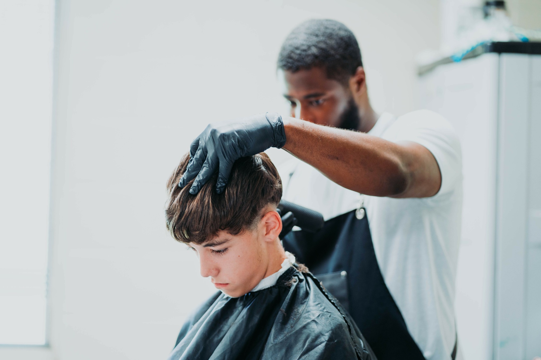 Barber cutting a young boy's hair in a salon, with the barber wearing gloves and focused on the haircut.