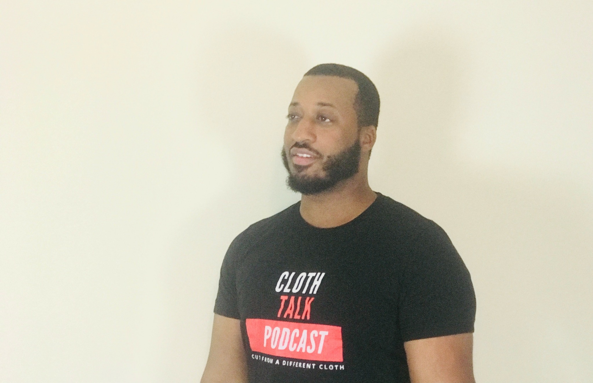 Man with beard and short hair wearing a black T-shirt with text, standing against a plain light background.