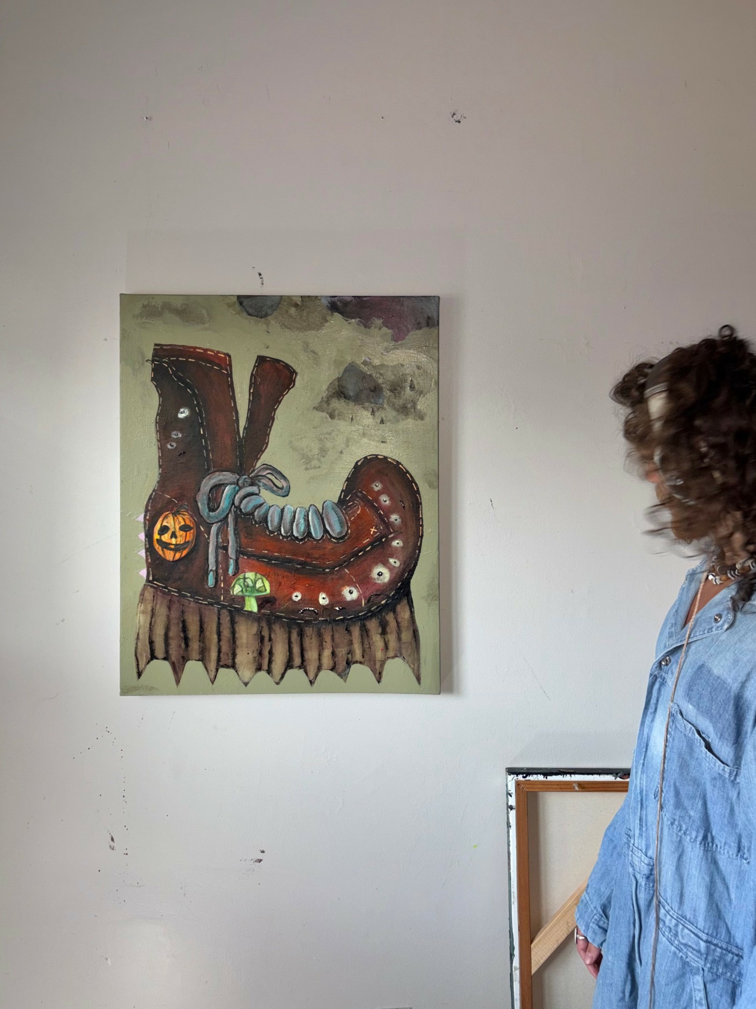 Person with curly hair wearing a blue jacket looking at a colorful, abstract artwork on a white wall.