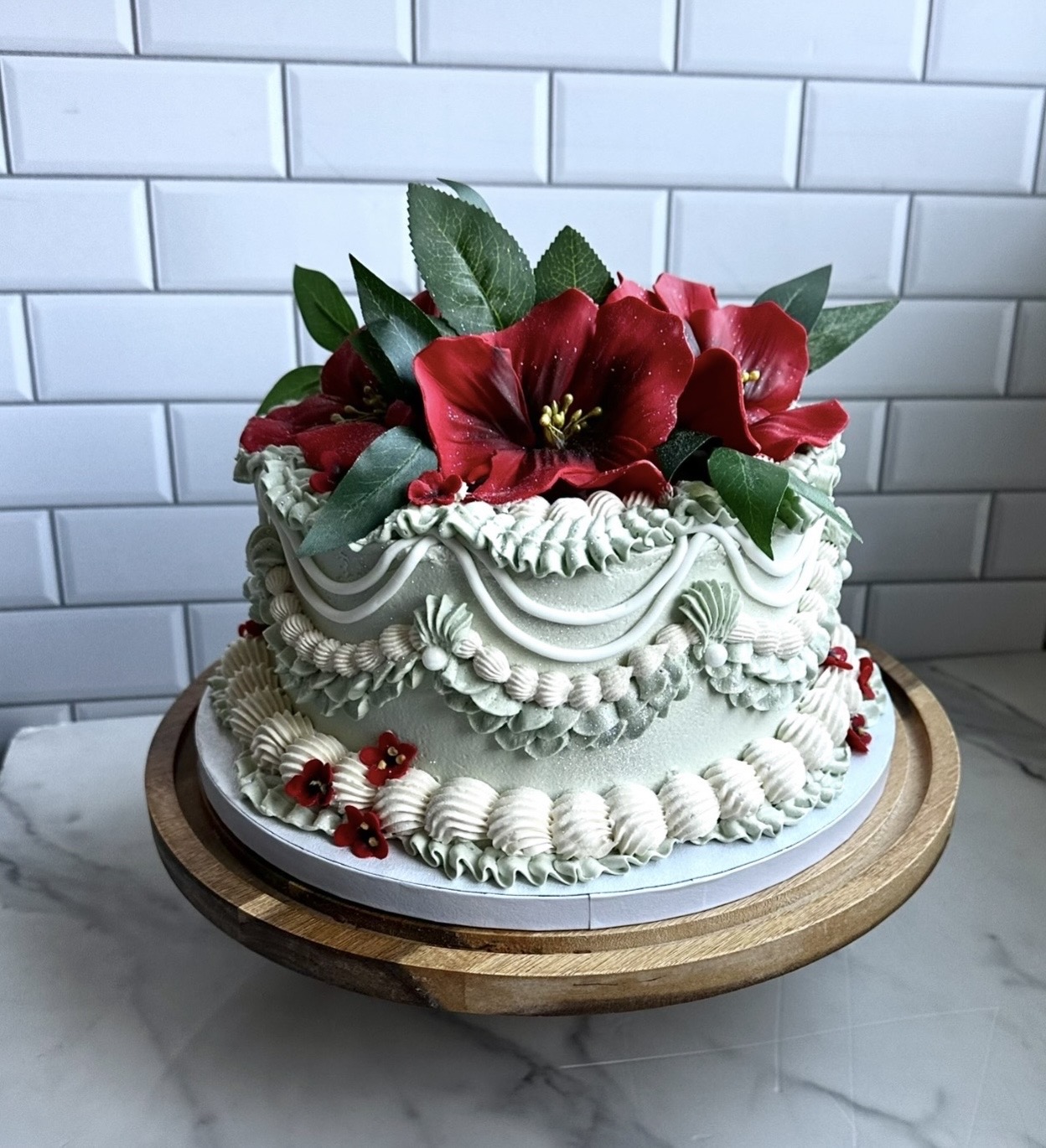 Decorative cake with red flowers and green leaves on top, white frosting with piped details, on a wooden stand.