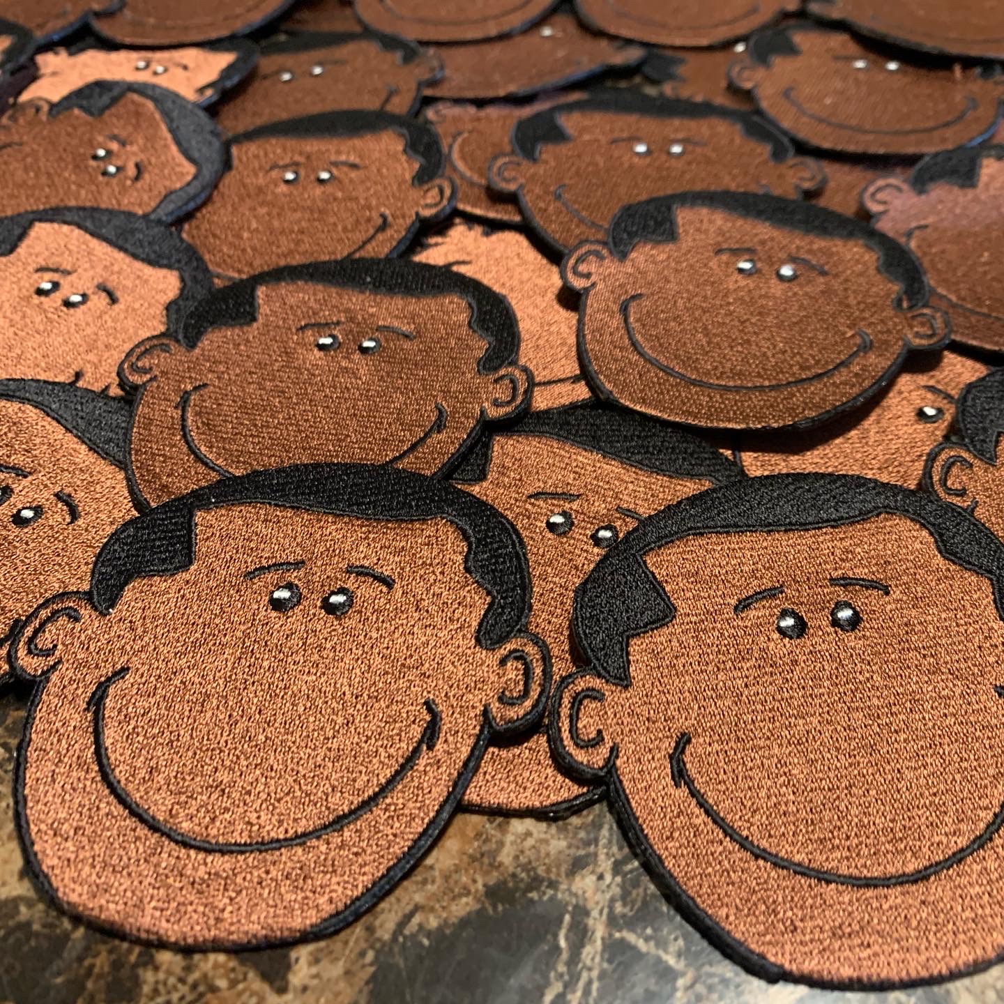 Multiple cartoon-style smiling faces with dark hair and simple features, overlapping each other, on a textured surface.