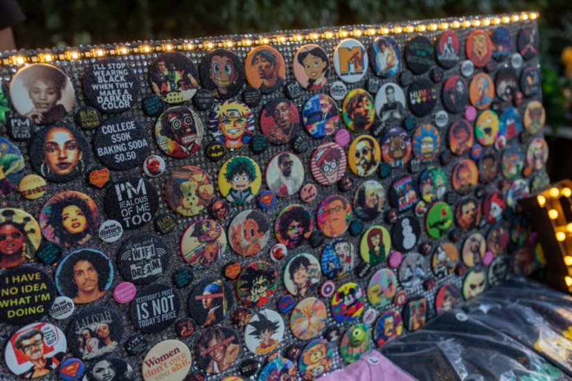 Display of colorful buttons with various designs and characters, illuminated by string lights, outdoors at night.