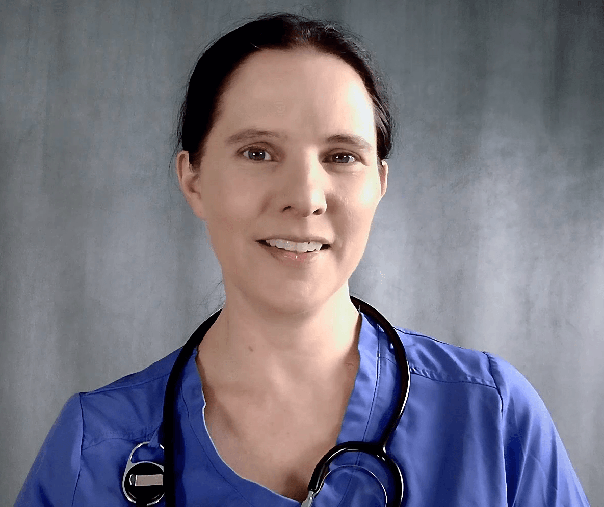 Woman in blue medical scrubs with stethoscope, smiling, against gray background.