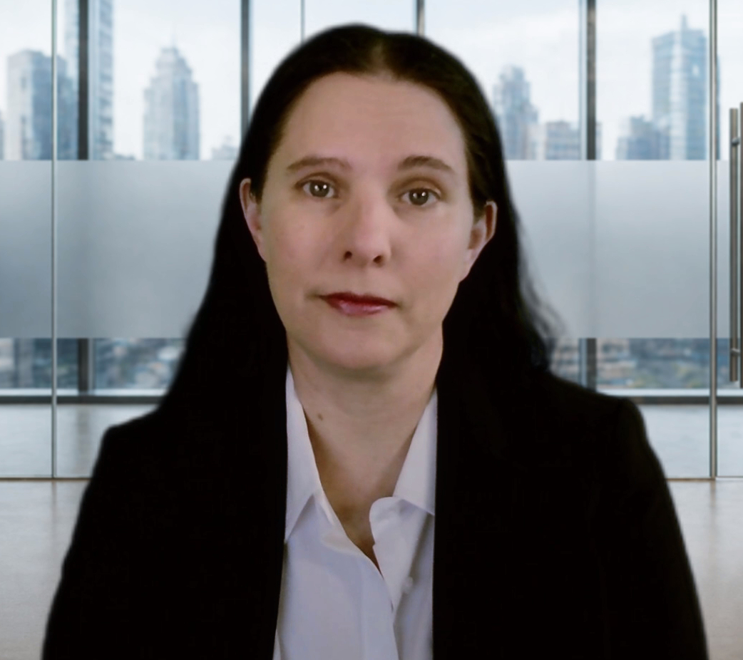 Woman with dark hair in a business suit in an office with city skyline view behind her.