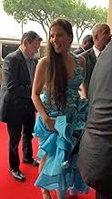 Group of people at an event, woman in blue dress smiling, red carpet, trees in background.