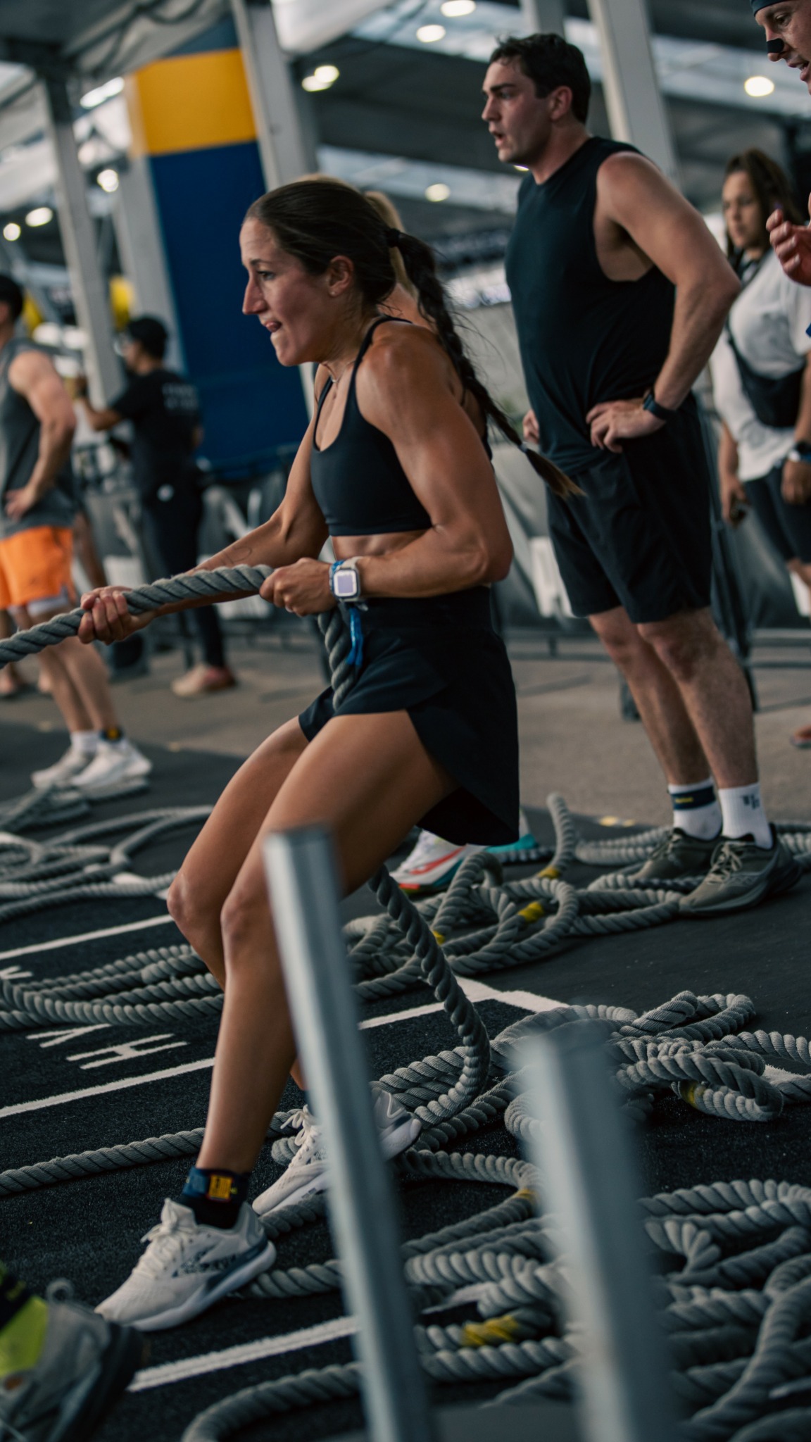 Woman pulling battle ropes in a gym with other people in the background.