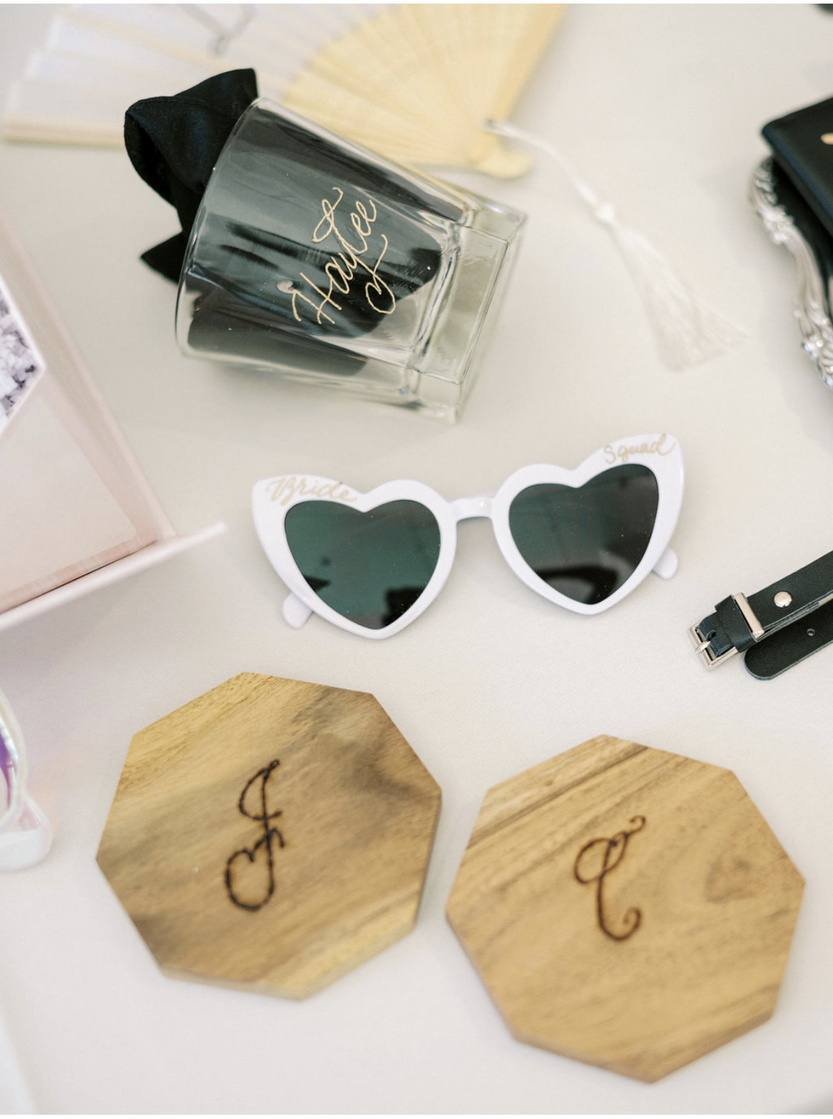 Sunglasses with heart-shaped white frame, perfume bottle, and wooden coasters on a white surface.