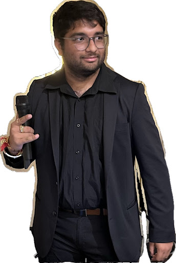 Man in black suit holding a phone, looking to the side, with glasses and dark hair.