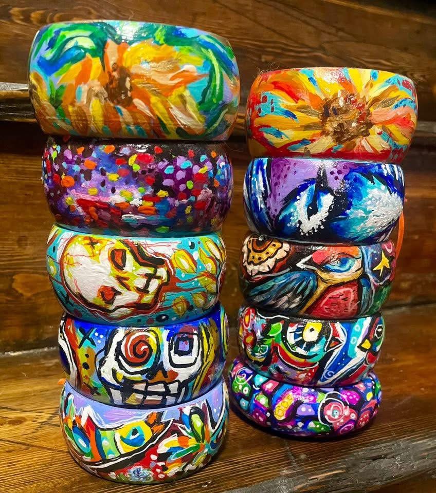 Stacked colorful painted rocks with abstract and whimsical designs on a wooden surface.