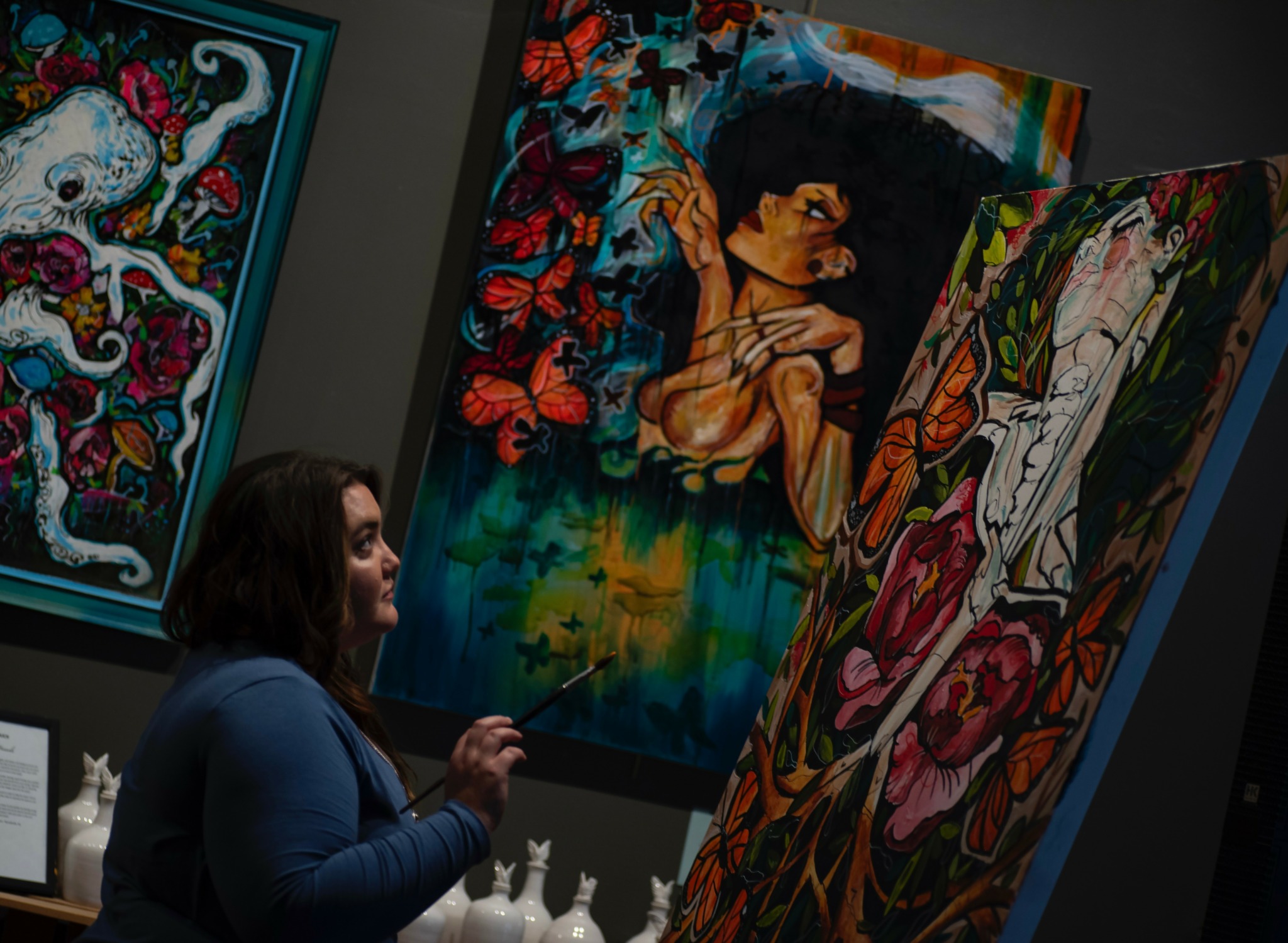 Woman observing colorful paintings in an art gallery, with vibrant abstract and floral artwork on display.