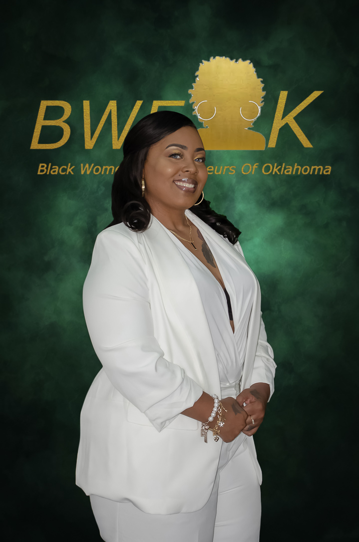 Woman in white suit smiling in front of a green background with text, no face visible.