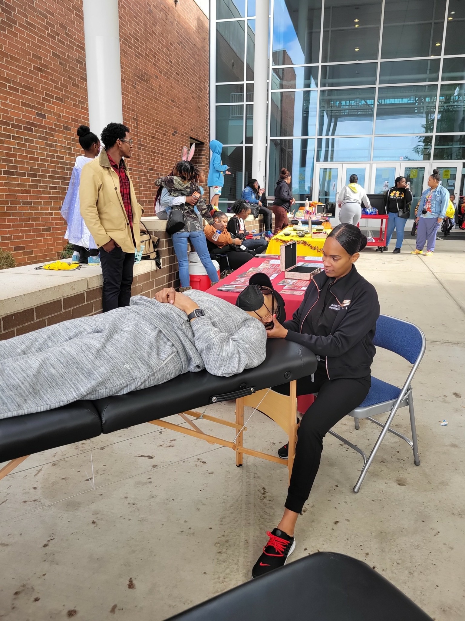 Person receiving a health checkup at an outdoor event with tables and people in the background.