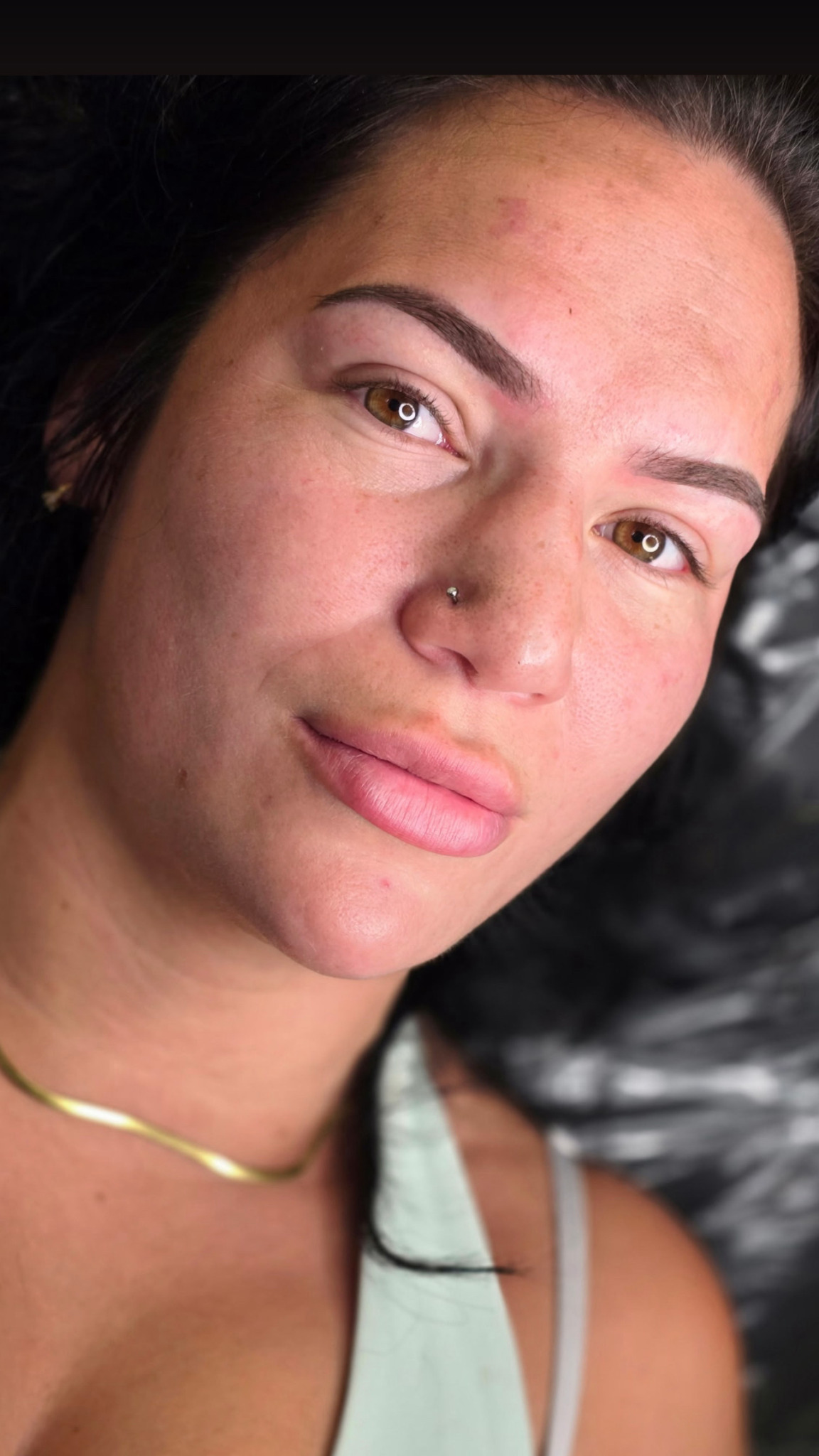 Close-up of a woman with dark hair, light skin, and a nose piercing, lying down with a neutral expression.