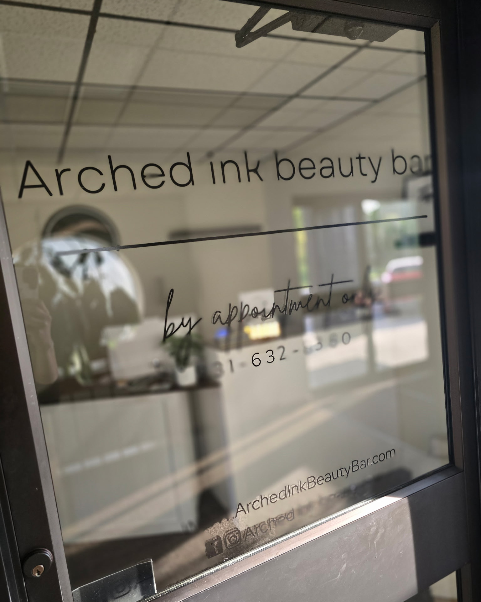 Glass door with text advertising Arched Ink Beauty Bar, including contact information and website.