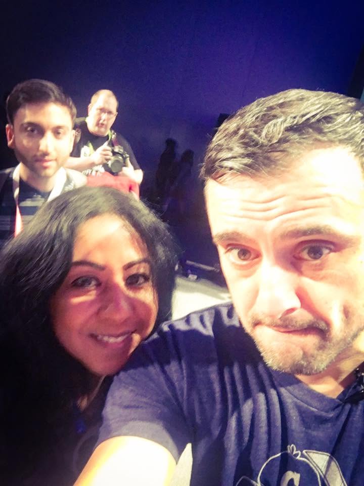 Four people taking a selfie, with a dark background and stage lighting, smiling and looking at the camera.