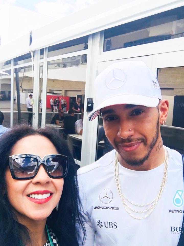 Two people smiling outdoors, one wearing sunglasses and the other wearing a white cap and gold chains.