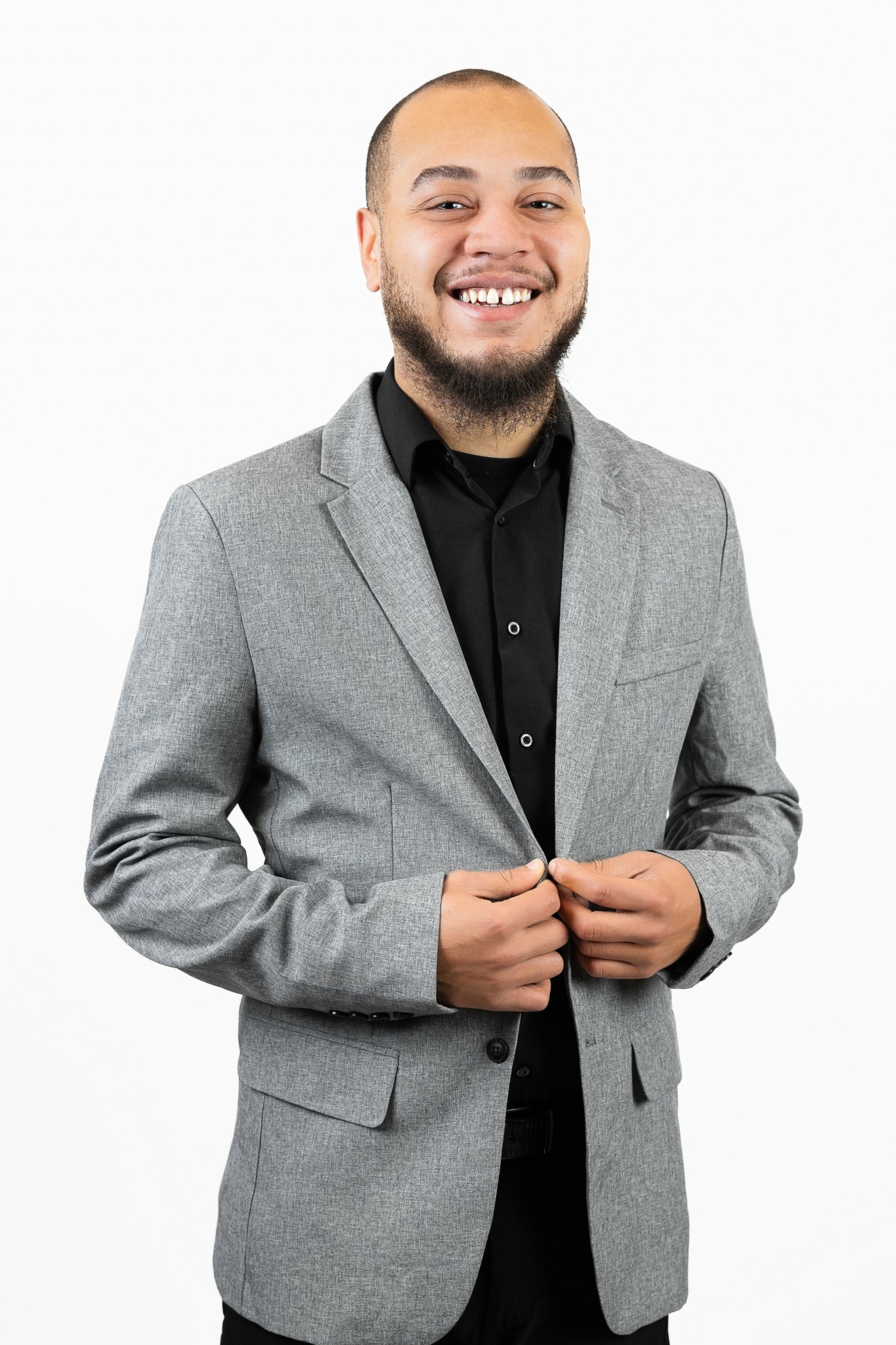 Smiling man in gray blazer and black shirt, standing against white background.