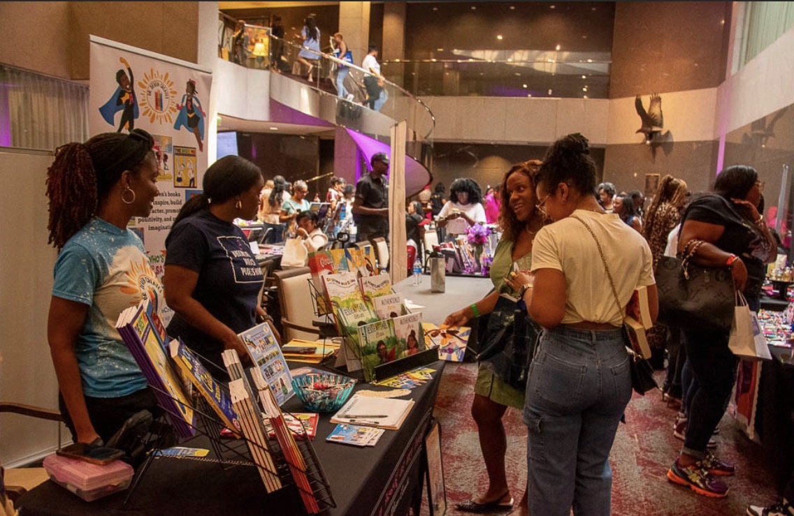 People browsing booths at an indoor event with displays and colorful lighting.