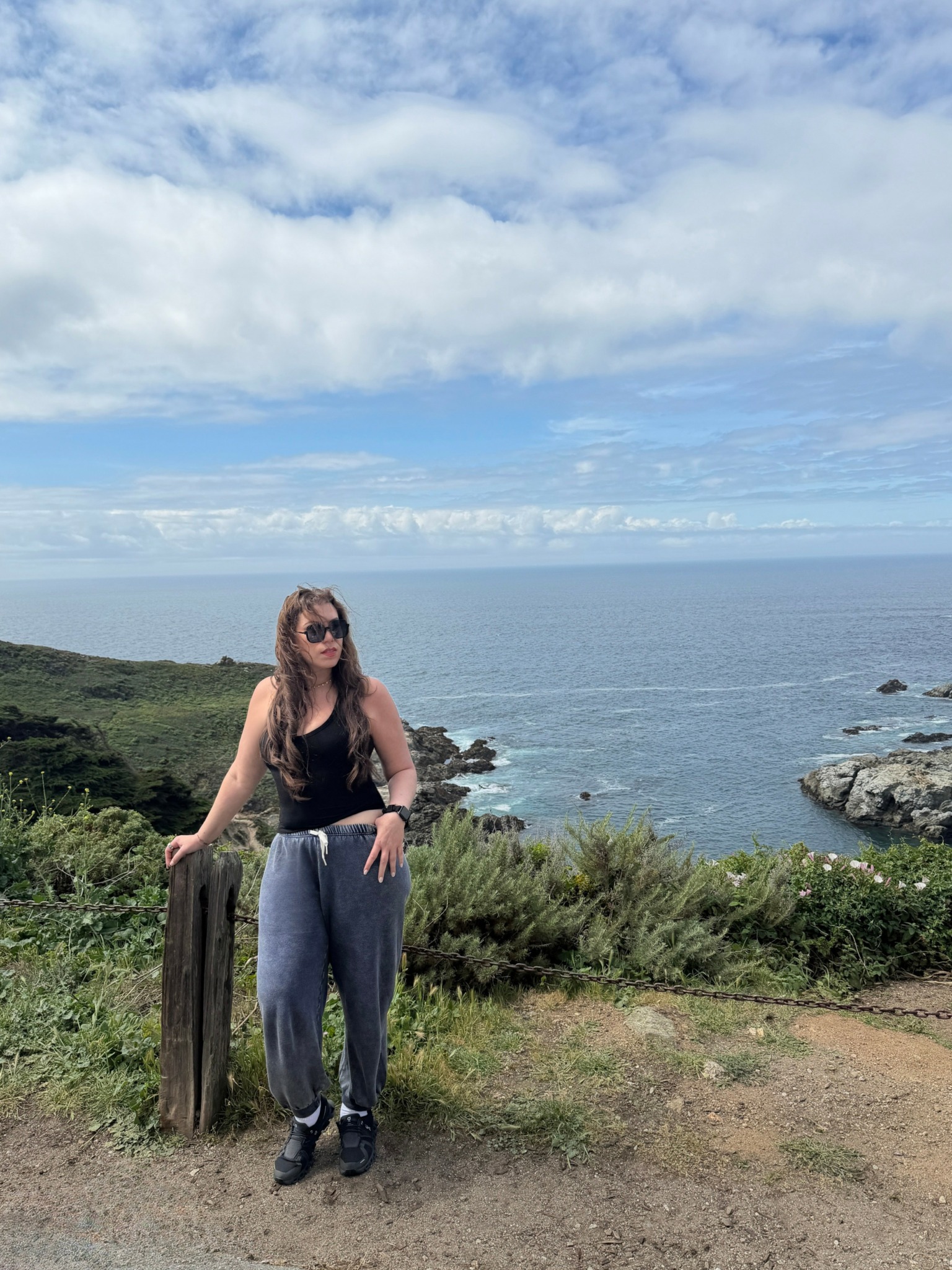 Woman standing outdoors near the coast with ocean and sky in the background.