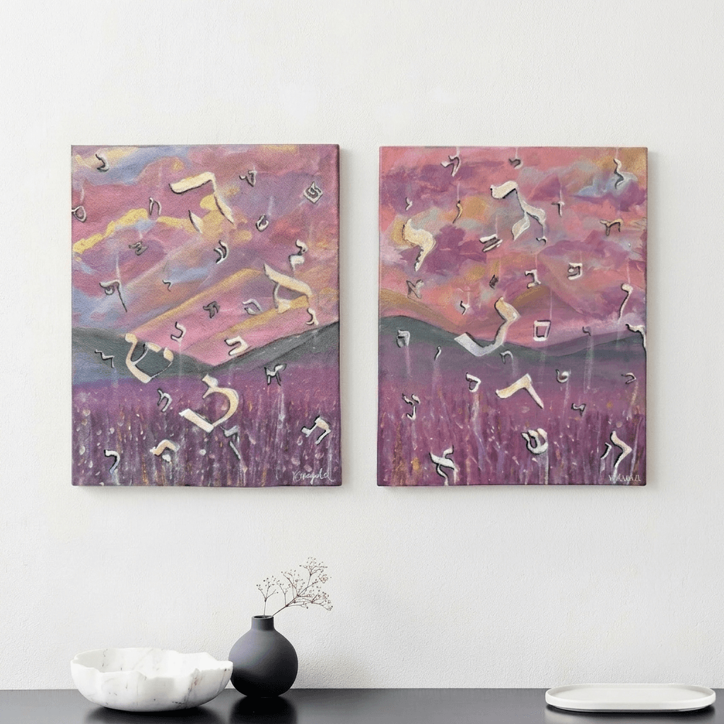 Two abstract landscape paintings with pink, purple, and yellow hues hang on a white wall above a table with a black vase and white bowl.