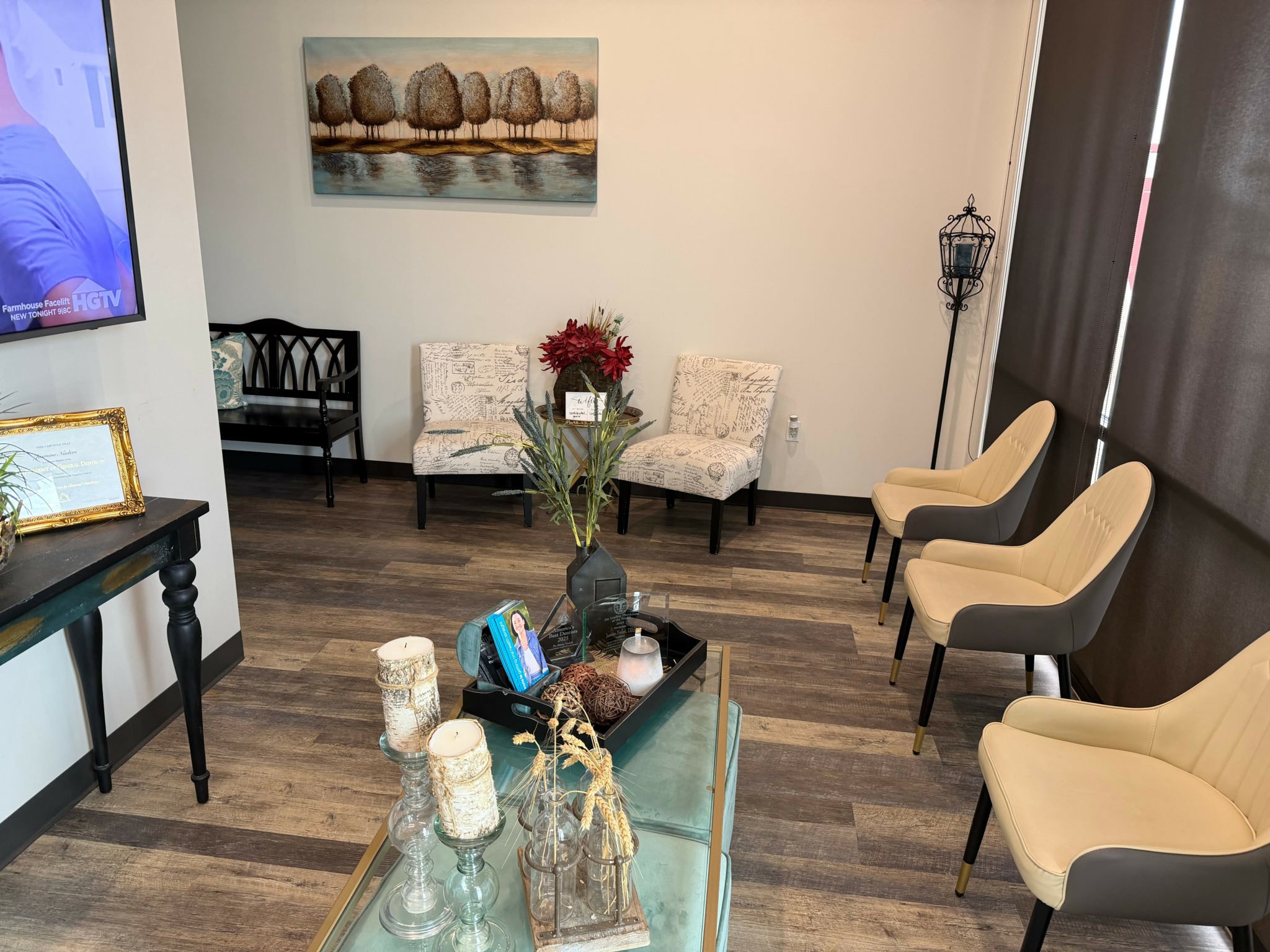 Living room with chairs, a table with decorative items, a painting, and a lamp. Wooden floor and curtains on the right.