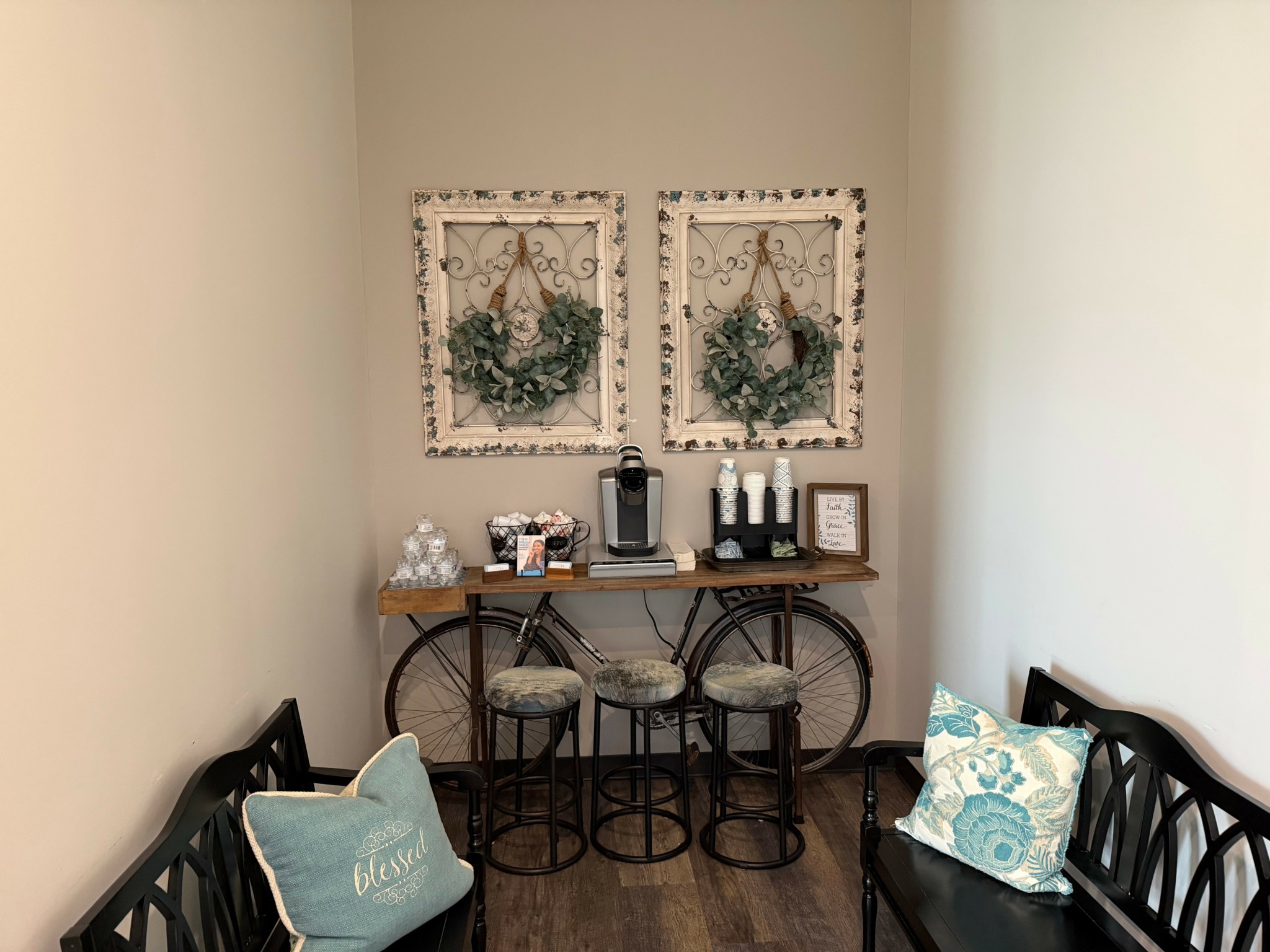 Small room with two framed wall decorations, a wooden table with decorative items, and two chairs with pillows.