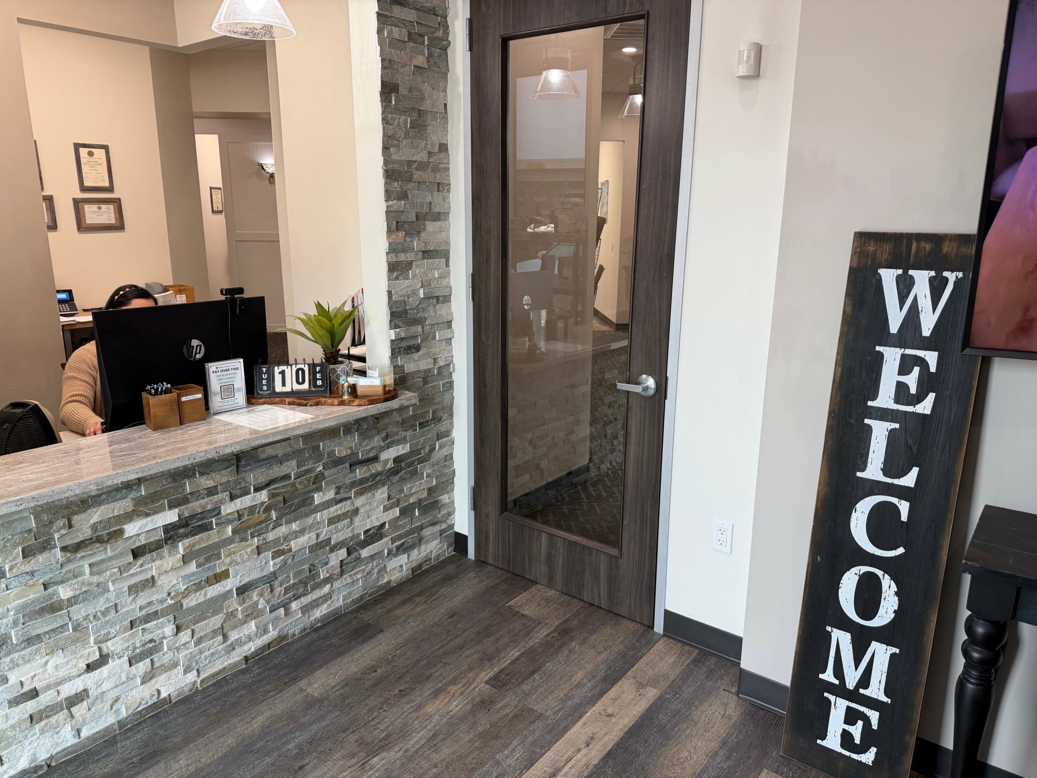 Interior of a reception area with a stone wall, wooden floor, glass door, and a welcome sign.