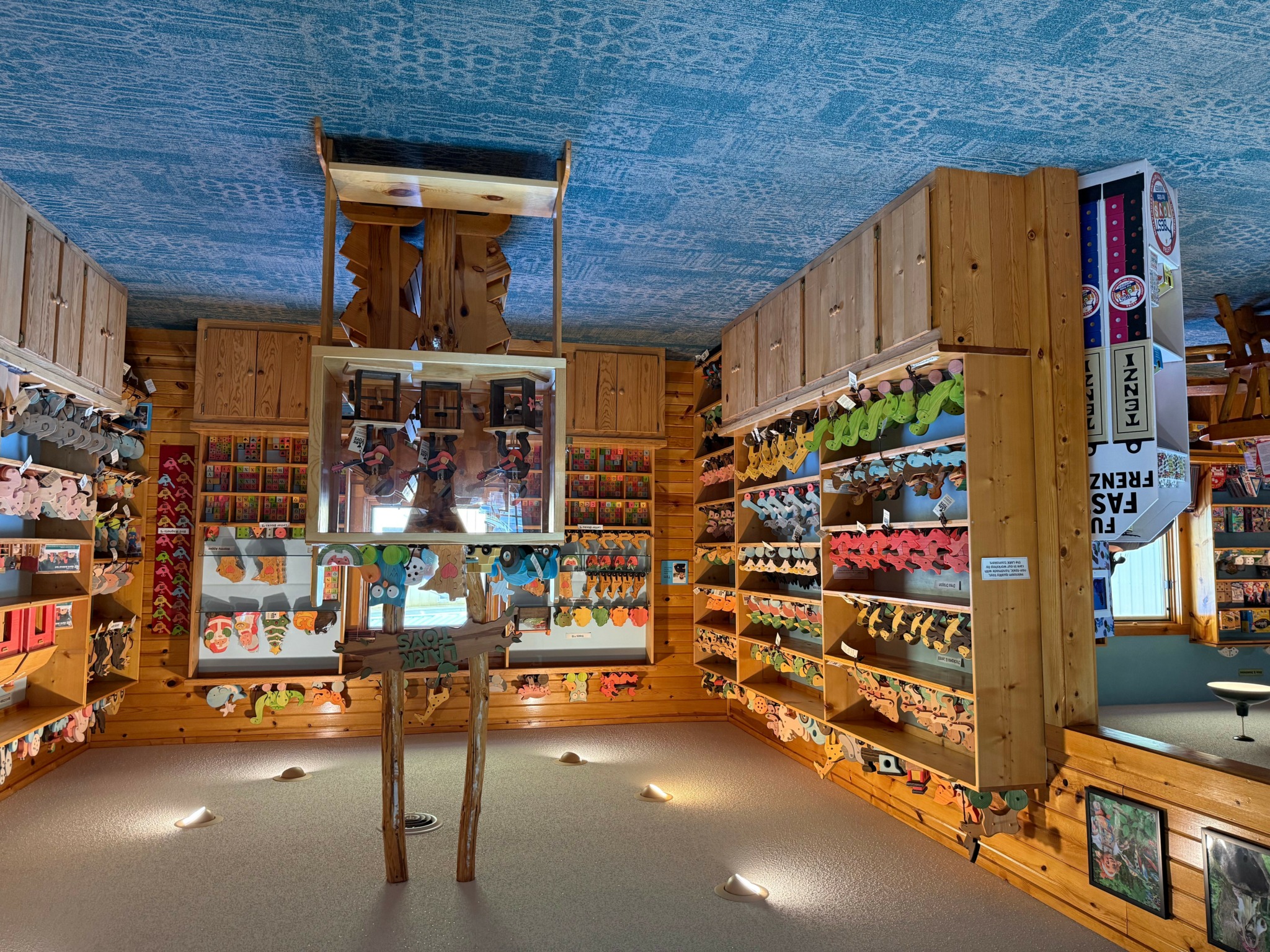 Indoor store with wooden shelves filled with colorful yarns and craft supplies, ceiling painted blue, and small spotlights on the floor.