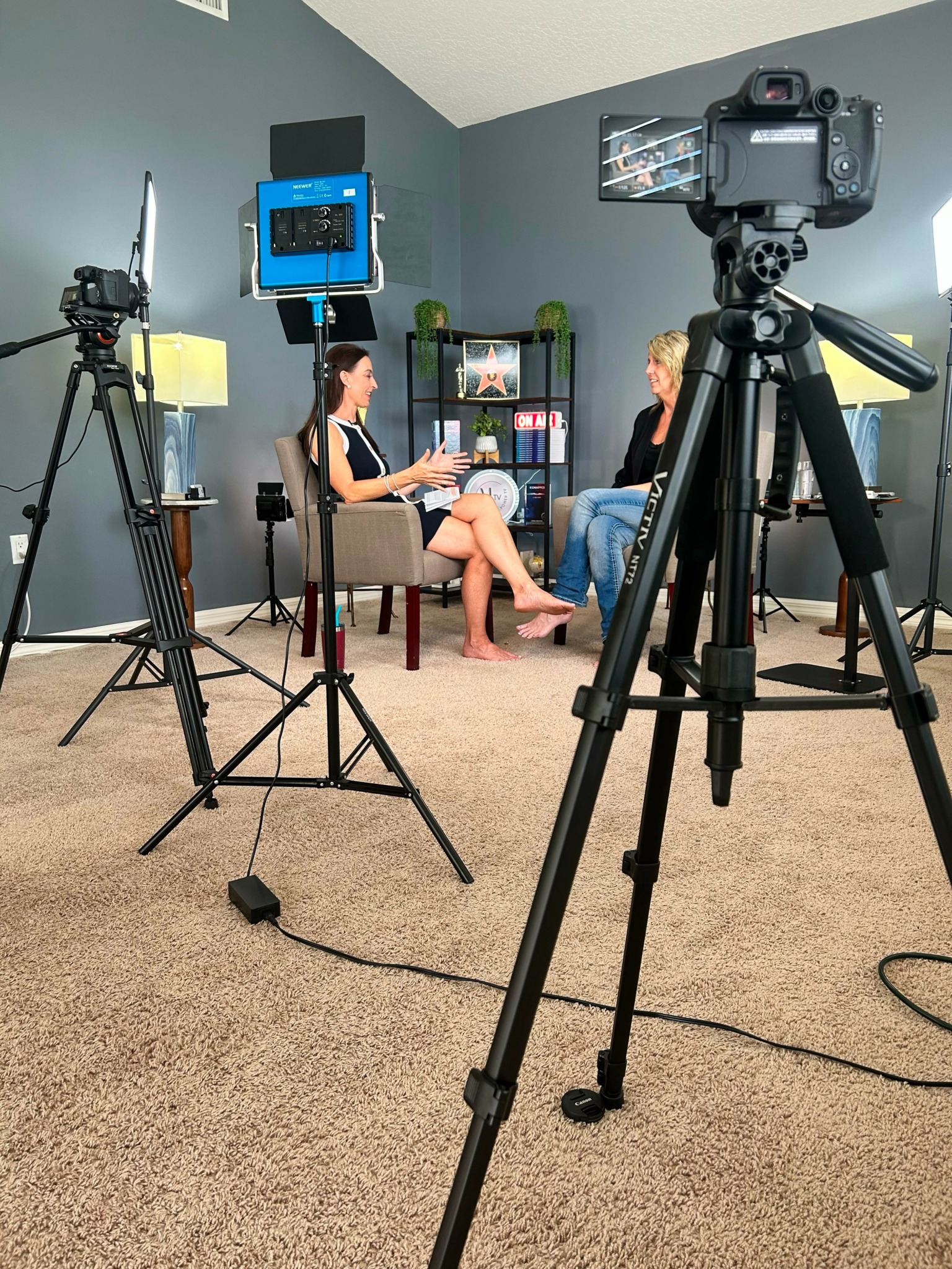 Two women sit in chairs facing each other in a room with cameras and lighting equipment, engaged in conversation.