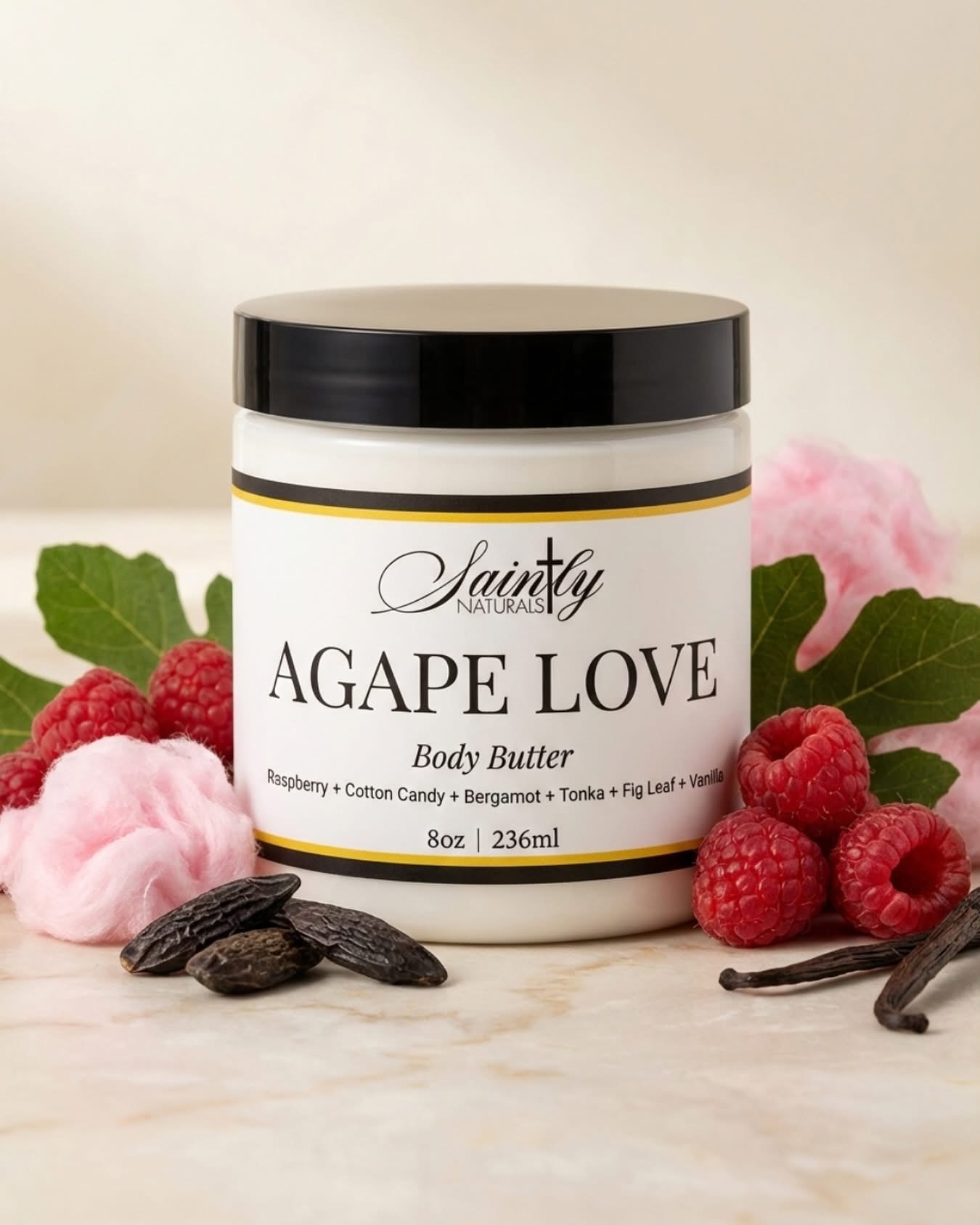 Container labeled 'Agape Love' body butter surrounded by raspberries, cotton candy, and vanilla beans on a light background.