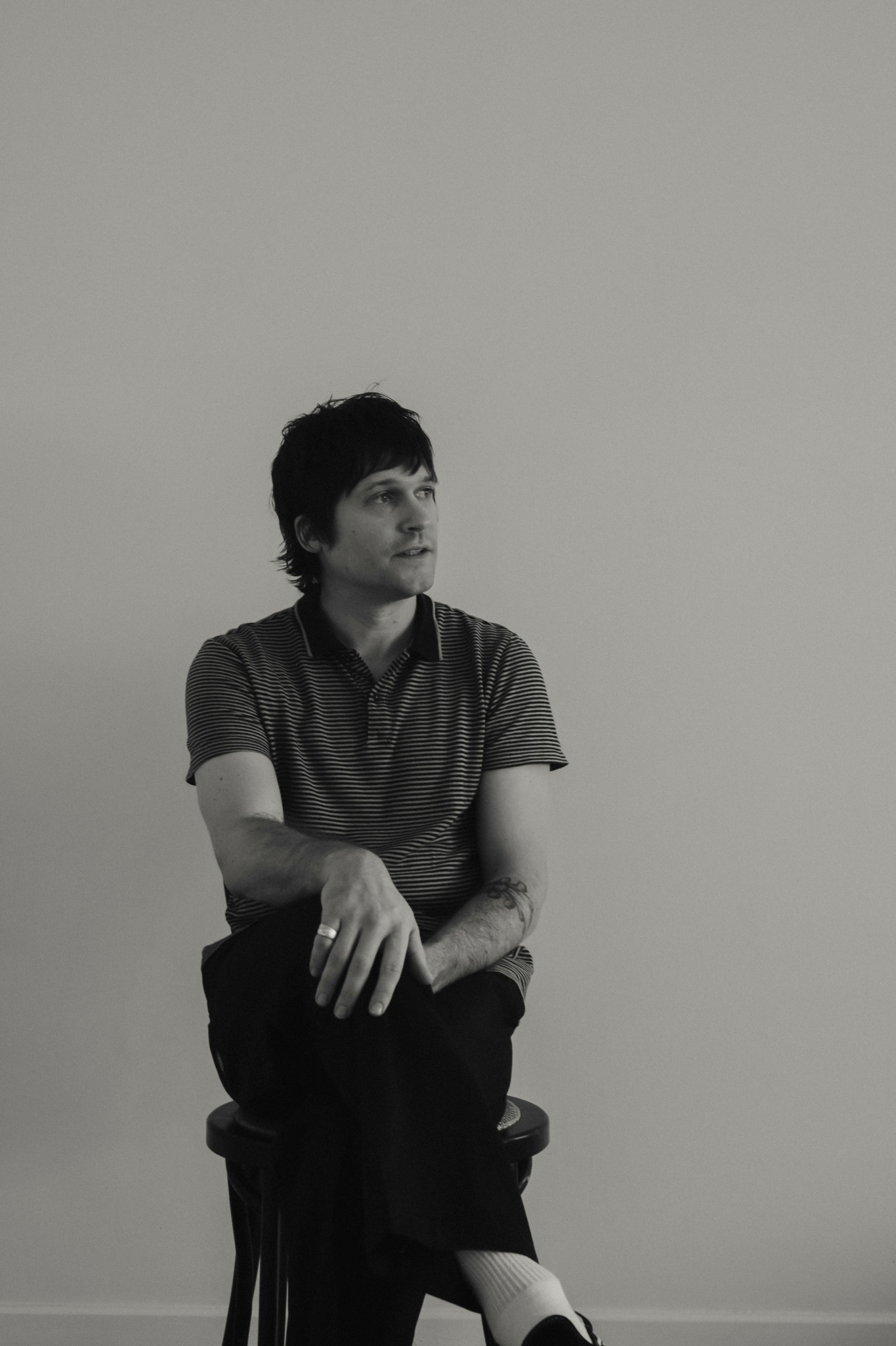 Person sitting on a chair against a plain wall, looking to the side, with arms crossed and legs crossed.