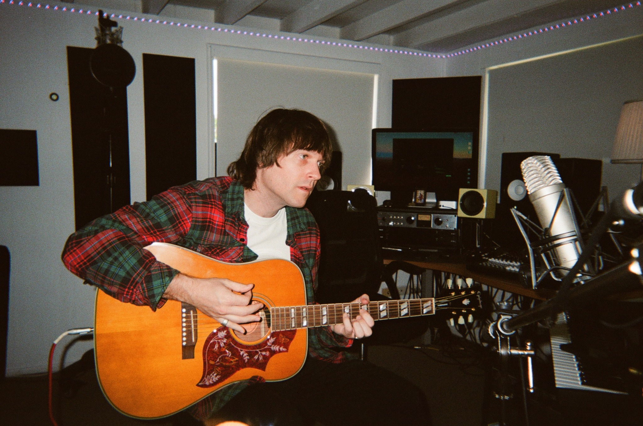 Person playing acoustic guitar in a recording studio with microphones and audio equipment.
