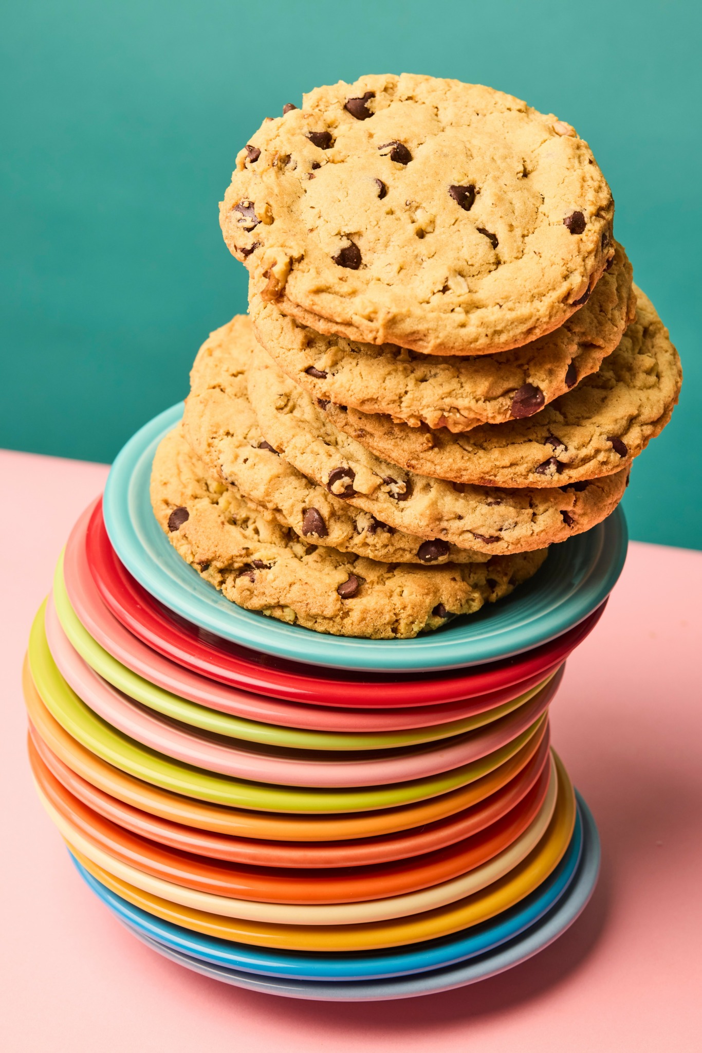 Stack of chocolate chip cookies on colorful plates against a teal and pink background.