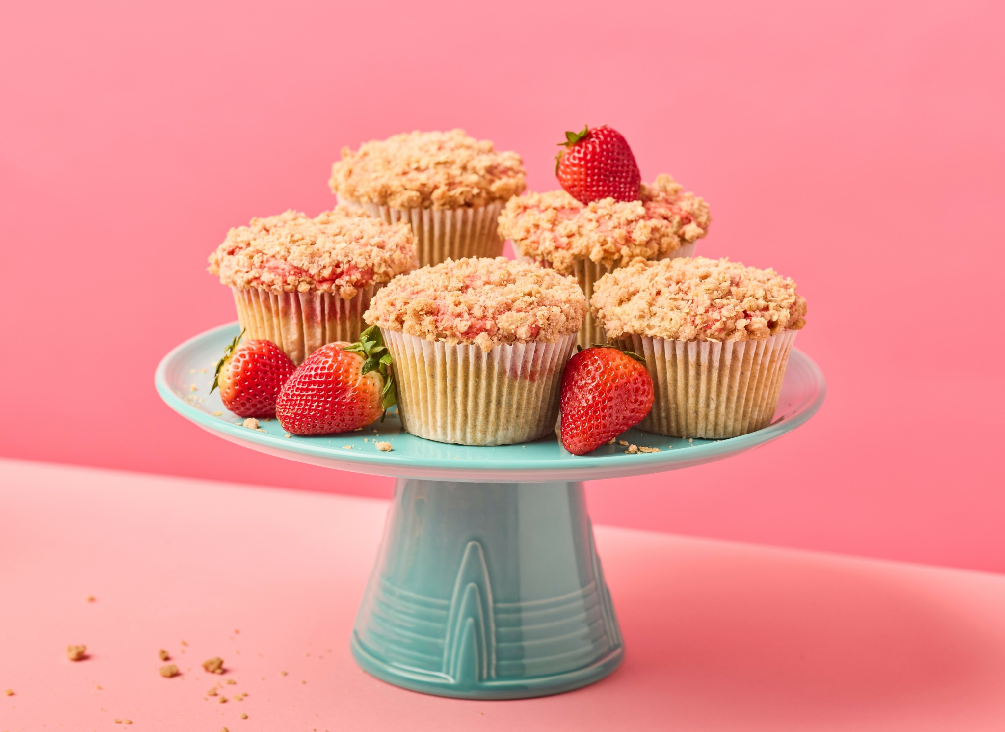 Six cupcakes with pink frosting and strawberries on a light blue cake stand against a pink background.