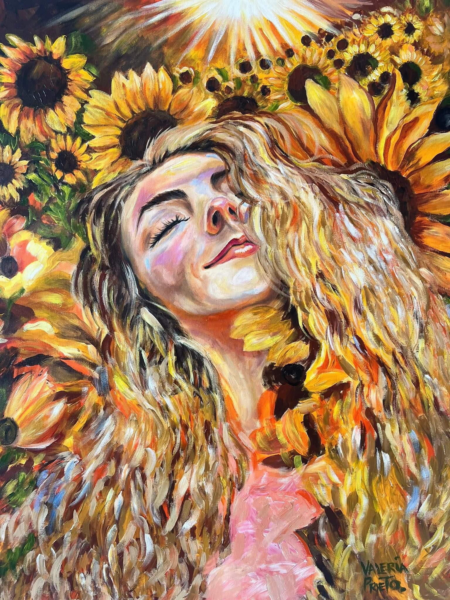 A woman with long, curly hair smiling with eyes closed among sunflowers and bright sunlight.